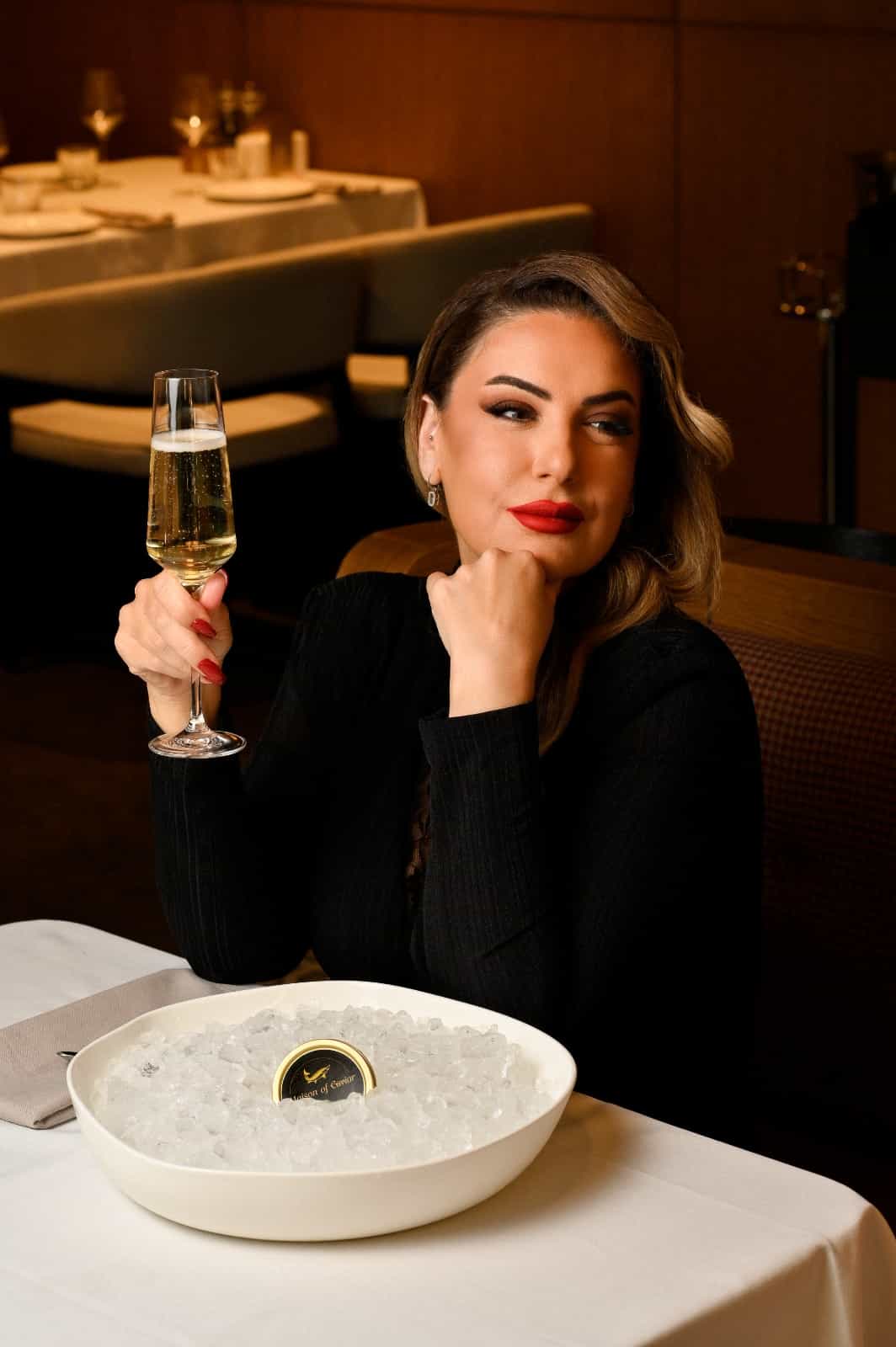 Nicole at a dinner table with a glass of champagne and a tin of Maison of Caviar on ice